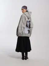 Buzo hoodie oversize de felpa de algodón color gris, con capucha y bufanda integrada que envuelve el cuello. Presenta cierre frontal y bolsillos canguro.