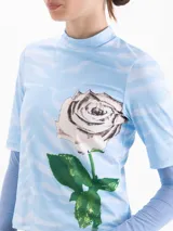 Top de cuello alto con mangas cortas, confeccionado en tejido de punto con estampado de efecto cielo y una rosa grande en el frente. Presenta un diseño entallado al cuerpo.