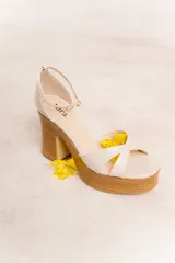 Sandalias color crema con tiras cruzadas y tobillera con hebilla dorada. Plataforma y taco de madera con diseño acanalado.