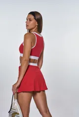 Conjunto deportivo de dos piezas compuesto por un top deportivo con escote redondo y una pollera short con abertura frontal, ambos en color rojo con detalles en blanco.