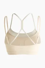 Top deportivo color beige claro con dos pares de tirantes finos en contraste y diseño de espalda cruzada.