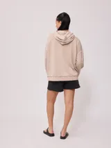 Canguro Rusty con capucha y efecto lavado color beige, de corte oversize, con bolsillo tipo canguro frontal, cordones ajustables y parche de la marca en el pecho. Presenta costuras expuestas y detalles deshilachados.