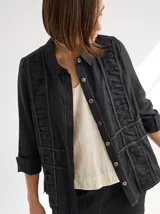 Camisa negra de lino con corte femenino, cuello clásico, cierre frontal con botones y mangas 3/4 con puños. Presenta detalles de frunces en el frente.