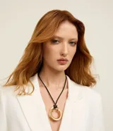 Collar corto de bisutería con cordón negro ajustable y un colgante circular dorado de diseño orgánico y acabado brillante.