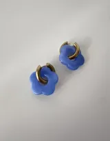 Aros de acero quirúrgico con argollas doradas y dijes colgantes en forma de flor de acrílico color celeste.