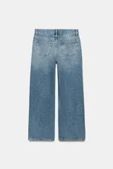Jeans wide leg de tiro medio confeccionado en denim con efecto lavado, corte relaxed y diseño de pernera ancha. Cuenta con cinco bolsillos, trabillas en la cintura y cierre frontal con cremallera y botón metálico. Presenta aplicación de brillos en toda la prenda.
