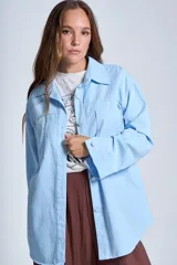 Sobrecamisa color beige confeccionada en gabardina, de corte holgado, con cuello camisero, cierre frontal con botones, dos bolsillos de parche en el pecho y mangas largas con puños abotonados.