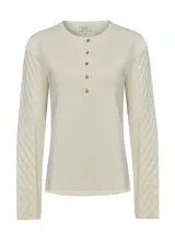 Remera de manga larga en color blanco hueso, con cuello redondo y cierre frontal parcial con botones. Presenta un diseño de tejido trenzado con textura en las mangas y cuerpo liso.