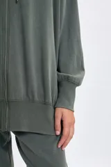 Campera deportiva de corte oversize con cierre frontal completo, capucha con cordones ajustables y puños elásticos. Presenta un acabado con efecto lavado en color verde.