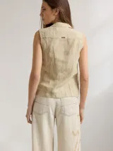 Camisa sin mangas de corte sastrero, color beige con textura arrugada y pespuntes en contraste. Presenta cuello solapa y cierre frontal con botones.