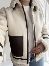 Chaqueta color crudo con interior de piel sintética color beige, cierre frontal con cremallera y un bolsillo de cuero marrón en el pecho.