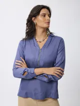 Blusa de satén color azul, con cuello camisero y cierre frontal parcial con cremallera. Presenta mangas largas con puños abotonados y un corte recto y fluido.