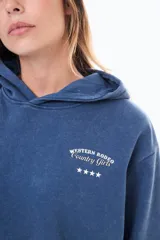 Buzo con capucha de felpa en color azul con efecto lavado. Presenta una estampa en la espalda con el texto 'WESTERN RODEO Country Girls' y cuatro estrellas blancas alineadas debajo.