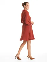 Vestido corto color terracota, confeccionado en crepe, con cuello camisero, escote en V y cierre frontal parcial. Presenta bolsillos decorativos con cierres metálicos en el pecho, mangas largas regulables con presillas y cintura elastizada.