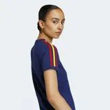 Remera de algodón azul marino de corte clásico y cuello redondo. Presenta las tres franjas características de Adidas en los hombros y mangas en colores rojo, amarillo y marrón. El logo del trébol de Adidas se encuentra bordado en color dorado en el pecho.