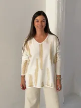 Sweater de punto con cuello en V y mangas largas, de diseño holgado. Presenta un estampado abstracto con pinceladas en color dorado sobre una base blanca.