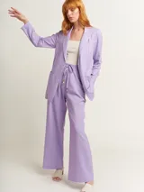 Blazer oversized lila de corte recto, largo a la cadera, con hombreras finas forradas, costuras internas con sesgo combinado y maxi bolsillos delanteros. Incluye lazo de algodón con detalle a tono.