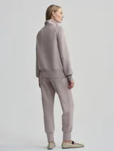 Campera deportiva con cierre frontal, cuello alto tipo chimenea y mangas raglán. Es de corte holgado y presenta bolsillos de parche delanteros. El color es un tono neutro entre gris y rosado (taupe).