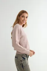 Buzo de tejido de punto en color rosado, con cuello redondo, mangas largas y puños acanalados. Presenta un diseño de tejido texturizado en la parte inferior y en los puños.