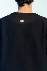 Buzo de felpa negro de corte oversize, con cuello redondo y mangas largas con puños grises doblados hacia afuera. Presenta costuras externas decorativas en tono gris claro a lo largo de las mangas y los hombros.