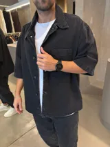 Camisa de jean en color negro lavado, con corte boxy, mangas cortas, cuello clásico y bolsillo frontal en el pecho.