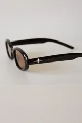 Lentes de sol con armazón ovalado de color negro y cristales tonalidad marrón. Presentan un detalle metálico en forma de estrella en las patillas.
