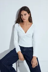 Top de manga larga blanco con escote en V y detalle de nudo fruncido en el centro del pecho.