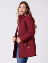 Campera capitoneada de largo midi en color bordó, con diseño de rombos en el cuerpo y mangas, y costuras diagonales en los laterales. Cuenta con cierre frontal, capucha desmontable con interior suave y panel entallado en la cintura.