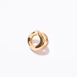 Anillo de metal dorado con diseño orgánico y voluminoso, con una forma irregular y curva que simula un nudo o un aro retorcido.