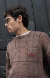 Buzo tejido de punto con diseño geométrico de cuadrillé en tonos azul y verde. Presenta cuello redondo, mangas largas y un parche de cuero sintético con logo en el pecho.