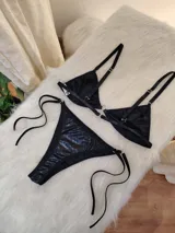 Conjunto de bikini negro de cuerina texturizada, con corpiño triangular con aro metálico central y bombacha colaless con tiras laterales ajustables.
