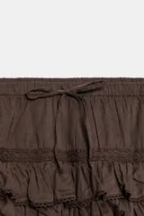 Shorts tipo pollera marrón de tiro medio, con cintura ajustable con cordones, diseño de múltiples volantes en capas y detalles de encaje a tono.