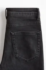 Jean de denim elástico color negro, de tiro alto, con cierre de botón y piernas acampanadas. Cuenta con bolsillos decorativos delanteros y bolsillos traseros.