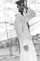 Blusa blanca confeccionada en lino, con cuello polo, escote en V y mangas largas amplias. Presenta un diseño holgado y bajo asimétrico.