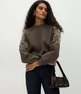 Buzo de moletón con felpa interna, cuello redondo y mangas raglán. Presenta bordados florales en las mangas y terminaciones acanaladas en puños y ruedo.
