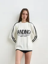 Buzo de punto blanco con rayas negras en las mangas y la inscripción "MANDINGA" y texto complementario en el pecho.