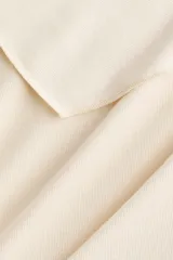 Top corto confeccionado en punto elástico de viscosa, color beige, con escote bote, hombros caídos y mangas cortas amplias. Presenta una sección superior superpuesta con un diseño asimétrico que crea un efecto capa.