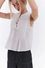 Blusa blanca sin mangas de algodón, con diseño de tablas frontales y escote con lazos para atar.