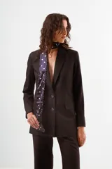 Blazer negro de corte clásico, con solapas de muesca, cierre frontal de un solo botón y bolsillos de ojal. Se combina con un pañuelo de seda azul marino con lunares blancos anudado al cuello.