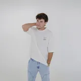 Remera color crema de corte holgado con cuello redondo y mangas cortas. Estampado pequeño en el pecho con texto en azul y amarillo.