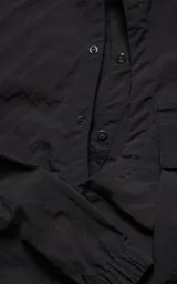 Chaqueta técnica liviana de microfibra con acabado mate, diseño con mangas desmontables que permiten convertirla en chaleco. Cuenta con cuello tipo camisa, cierre frontal oculto, cuatro bolsillos frontales de gran tamaño y puños elásticos. Incluye logo bordado en relieve en el pecho.