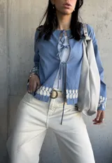 Chaqueta celeste con bordados florales blancos en el ruedo y los puños, con escote redondo y lazos para atar en el frente.