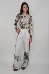 Pantalón de lino color celeste con estampado de palmeras en la parte inferior de las piernas y detalles de guarda pampa en color camel en los laterales. Tiene pretina y bolsillos.