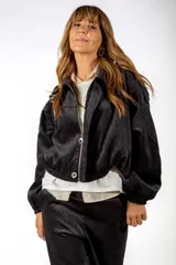 Campera corta de color negro con cierre frontal, cuello camisero y puños elásticos. Presenta un sutil estampado de textura animal print tono sobre tono.