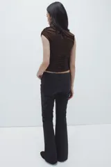 Top sin mangas color marrón oscuro, de punto elástico, con ajuste entallado. Presenta un adorno de metal y una tira larga en un hombro que forma un escote asimétrico. Los laterales están fruncidos para crear un efecto drapeado.