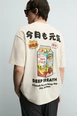 Camiseta relaxed fit color crema, con cuello redondo y manga corta. Presenta un estampado frontal con caracteres japoneses en negro y contorno rojo.