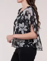 Blusa de gasa semitransparente con hilos de lúrex, diseño estampado floral en tonos blanco, gris y negro, silueta holgada tipo capa y escote redondo con detalle metálico.