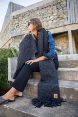 Chal largo tejido de punto grueso color gris oscuro con flecos en los extremos.