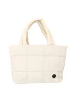 Bolsito tipo tote de diseño acolchado con costuras capitoneadas, color crema. Cuenta con dos asas superiores fijas, cierre principal y un pequeño aplique circular negro en la parte inferior.