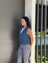 Chaleco de jean azul con cierre frontal mediante lazos ajustables, sin mangas y corte recto.